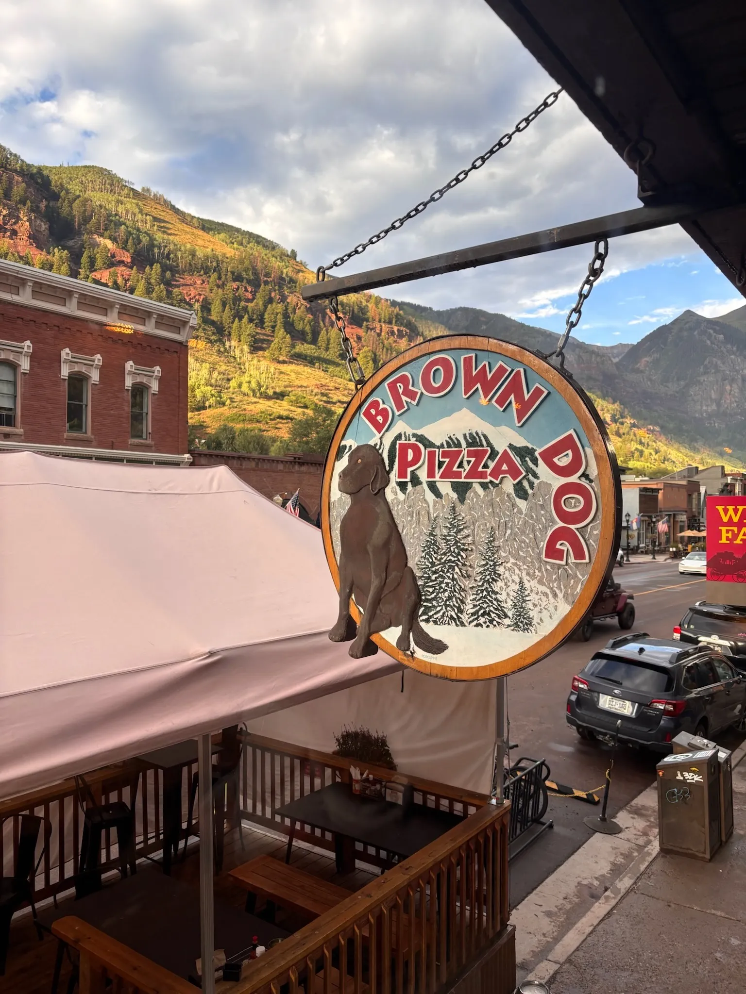 The Brown Dog Pizza sign over the patio, the hillside glowing behind it