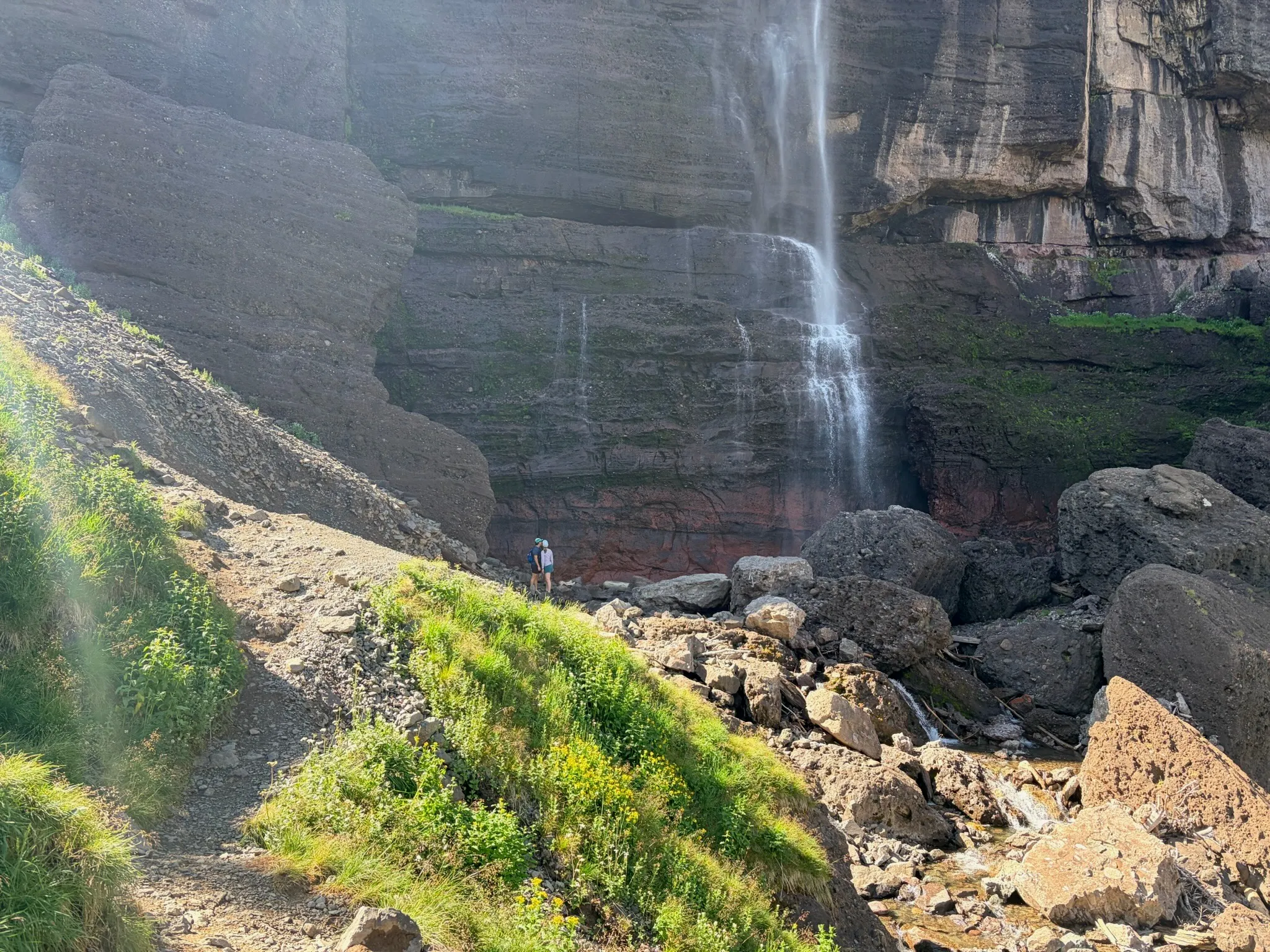 Morning sun flaring across the cliff face, the falls blowing sideways