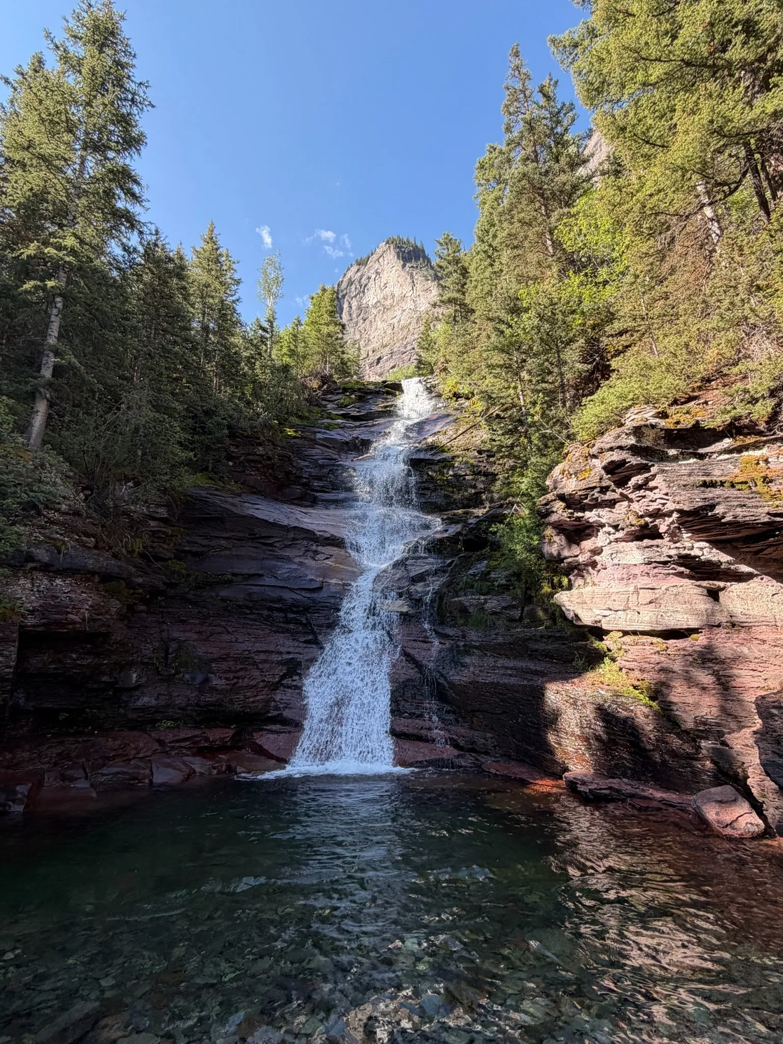 The falls dropping into a green pool ringed by red rock