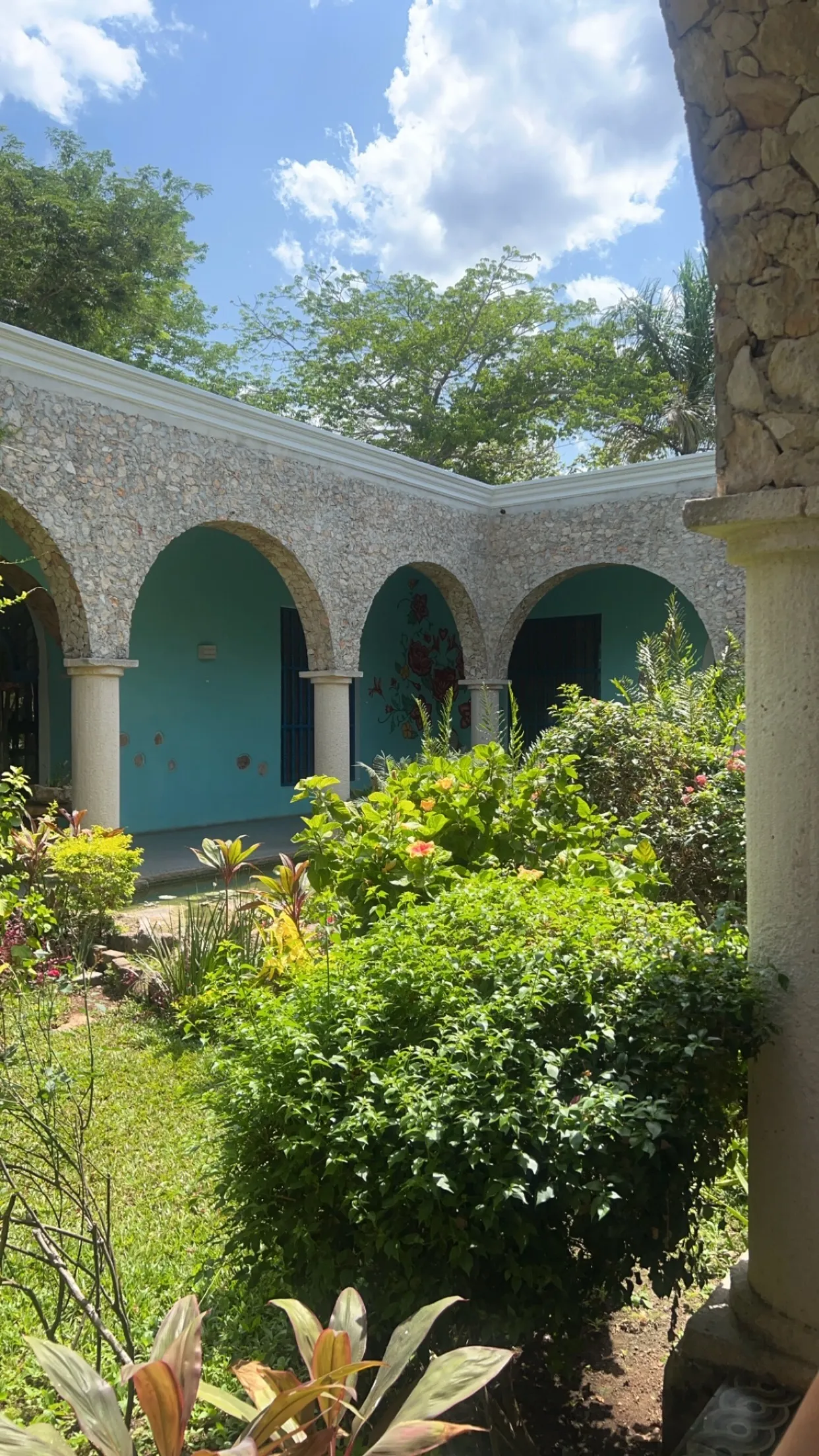 Teal courtyard walls and stone arches framed by garden and sky