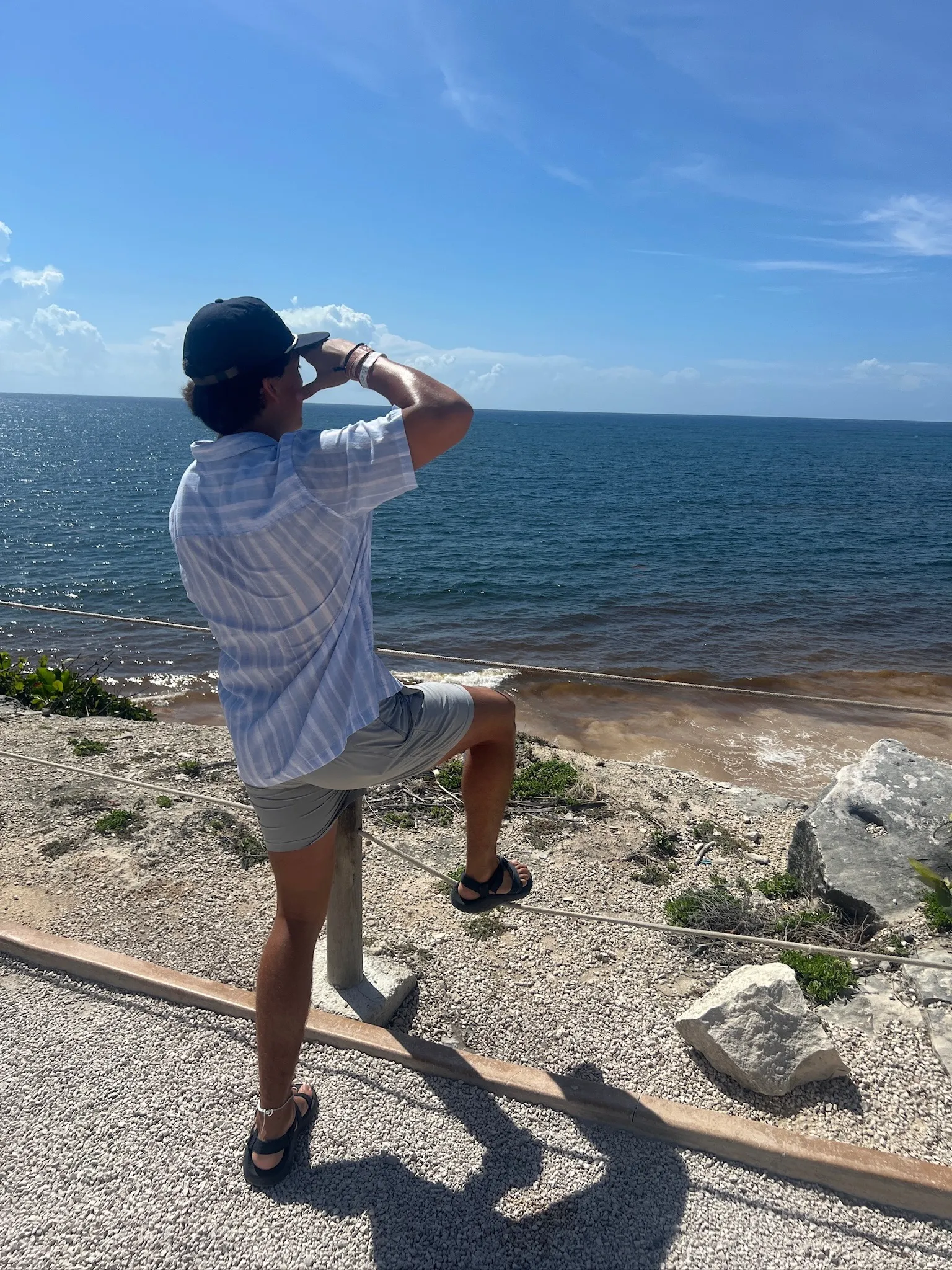 Looking out over the water from a rocky point, one foot up on the rope rail